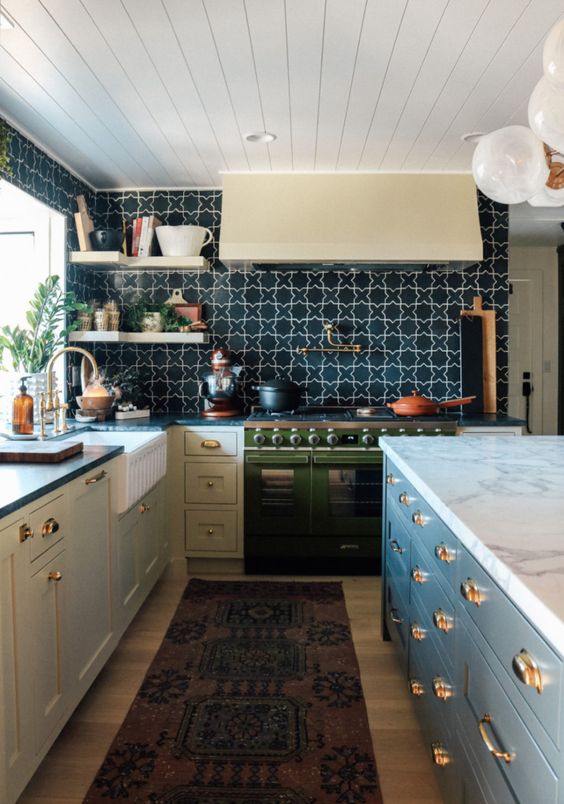 an eclectic kitchen with grey cabinets, a green cooker, a black and white printed tile backsplash, open corner shelves