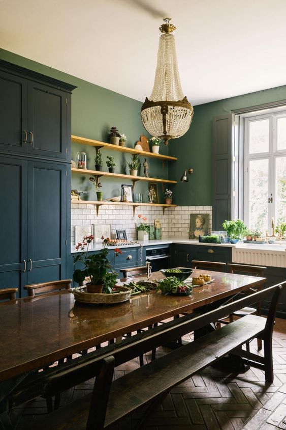 an eclectic kitchen with navy cabinets, green walls, a white subway tile backsplash, a dark-stained table and benches, a crystal chandelier