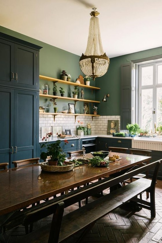 an eclectic kitchen with teal cabinets, green walls, white subway tiles, a crystal chandelier, a dark-stained table and benches and chairs