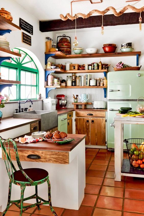 an eclectic kitchen with white and stained cabinets, a light green fridge, open shelves and pendant lamps, some shabby chic furniture