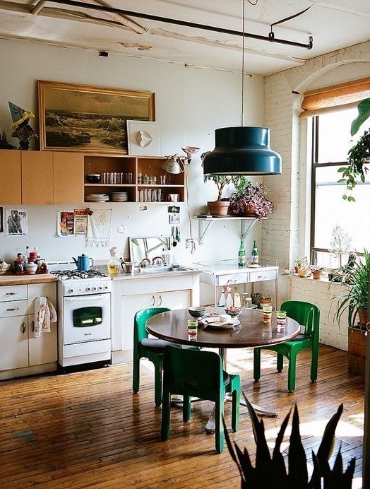 an eclectic kitchen with yellow and white cabinets, retro appliances, a round table, green chairs and a black pendant lamp