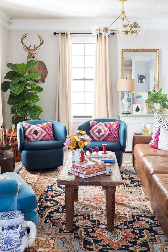 an-eclectic-space-with-folksy-and-boho-textiles-a-mid-century-modern-chandelier-a-leather-sofa-and-bright-blue-chairs.jpg