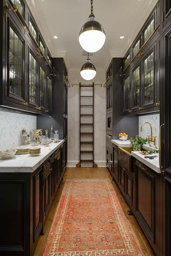 an elegant dark kitchen with traditional dark cabinets, a ladder to get things from upper cabinets and neutral stone countertops