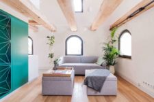 The living room is done with grey upholstered furniture, greenery and wooden beams on the ceiling