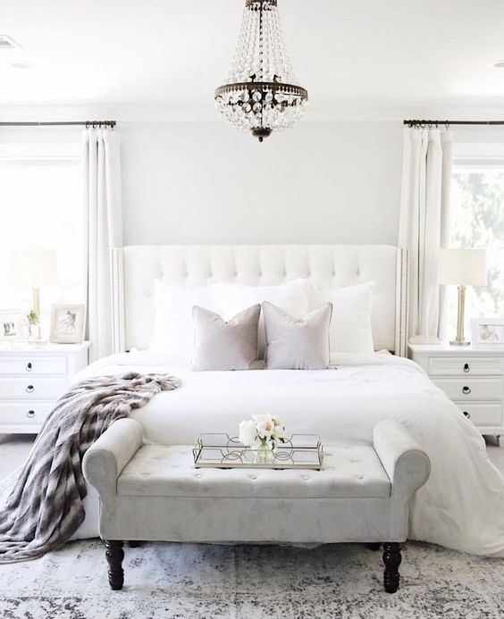 a chic bedroom in neutrals, with white walls, a white upholstered bed and a grey upholstered bench