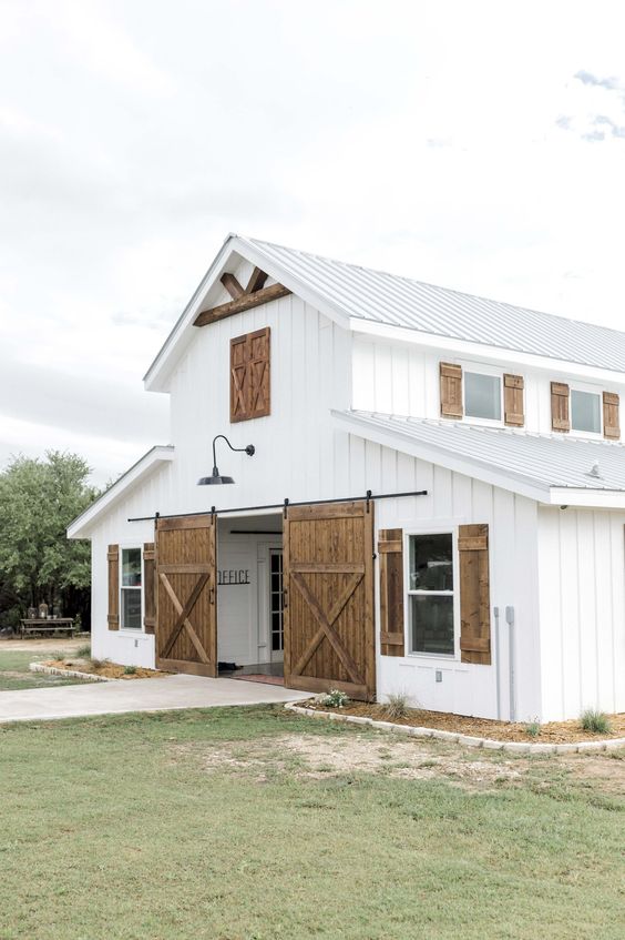 a large white barndominium with sliding barn doors done in a nautral stain of a light shade