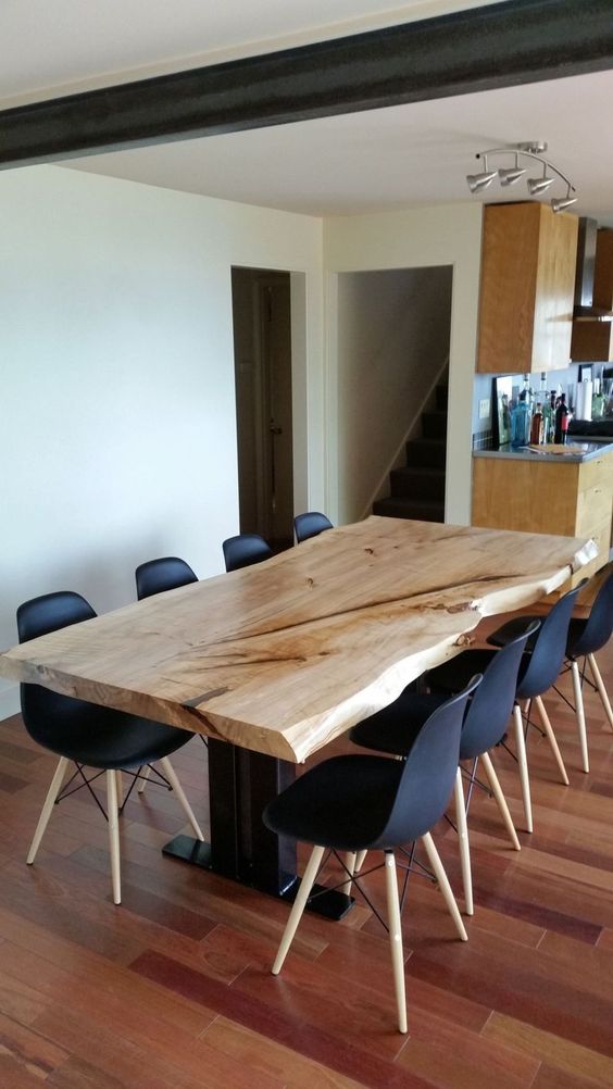 a laconic modern dining space with black chairs and a dining table with a live edge on black legs