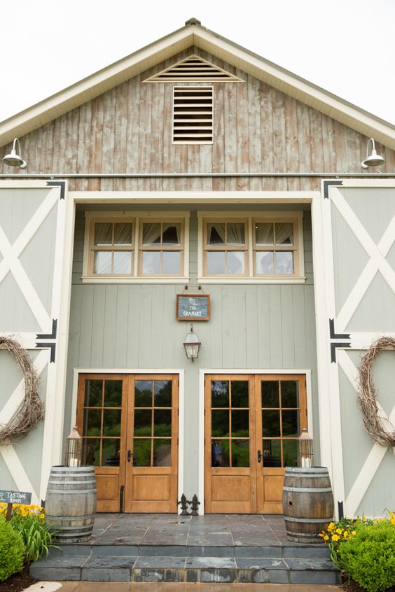 an awesome barndoiminium with oversized sliding barn doors, weathered wood on the facade and barrels by its side