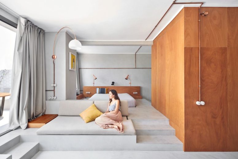 The bedroom features a bed on a platform, lamps and a large window and semalessly flows into a living room that flows into a terrace The bedroom features a bed on a platform, lamps and a large window and semalessly flows into a living room that flows into a terrace
