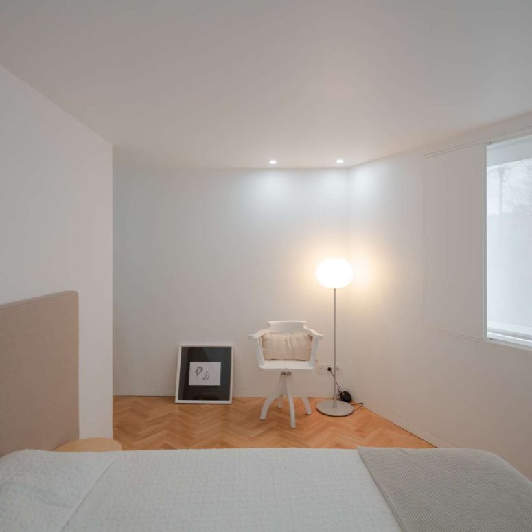 The bedroom is minimalist and neutral, with a floor lamp and a comfy bed