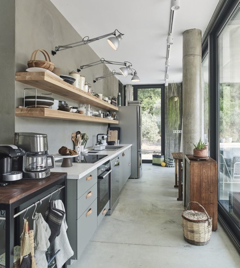 The kitchen feels pretty industrial, with grey furniture, wooden shelves, concrete floors and walls