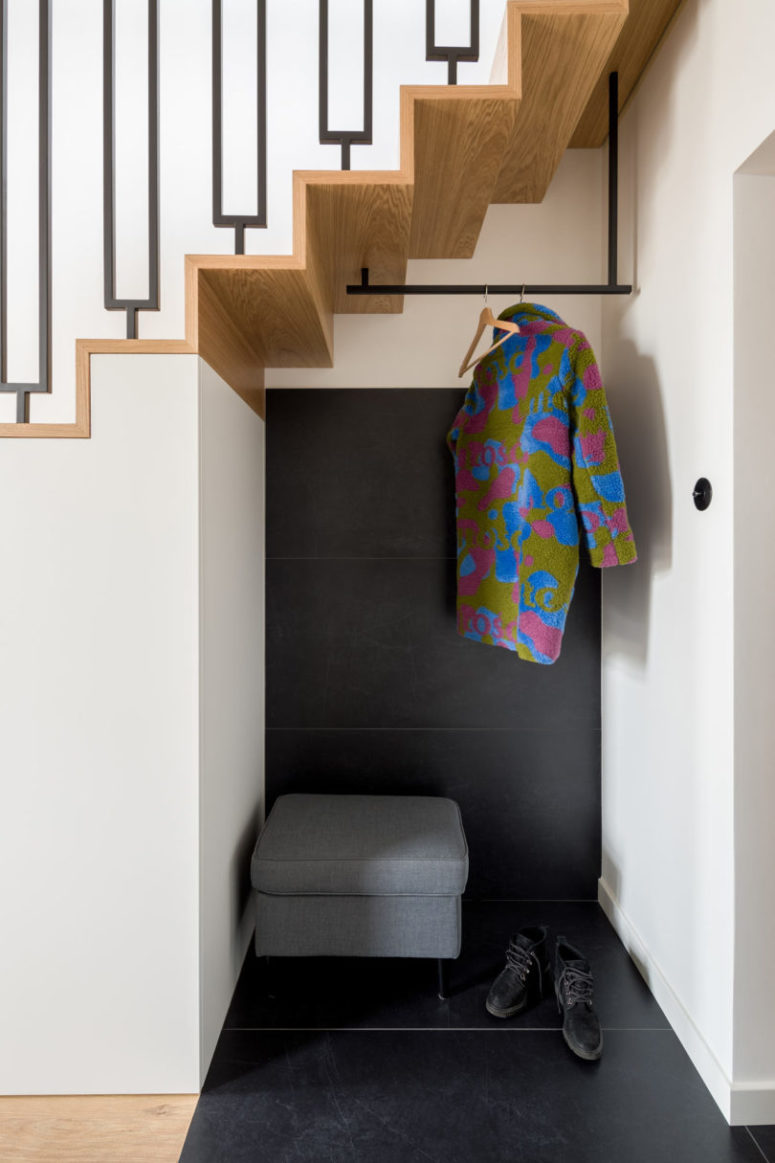 The tiny entryway nook is clad with black tiles, an upholstered seat with storage space and a clothes holder The tiny entryway nook is clad with black tiles, an upholstered seat with storage space and a clothes holder