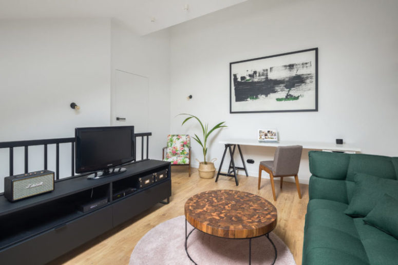 The living room is combined with a home office, there's a statement green sofa, a blush rug, a catchy table and a TV The living room is combined with a home office, there's a statement green sofa, a blush rug, a catchy table and a TV
