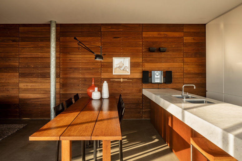 a warm wood mid century kitchen design The kitchen is clad with warm-colored reclaimed wood, with a stone countertop and there's a dining space with a wooden table and metal chairs
