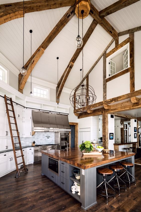 a white barndominium kitchen with wooden beams, pendant lamps, an oversized kitchen island