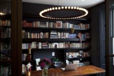 21 a black home office with bookshelves, a catchy modern chandelier, a wooden desk and a printed carpet