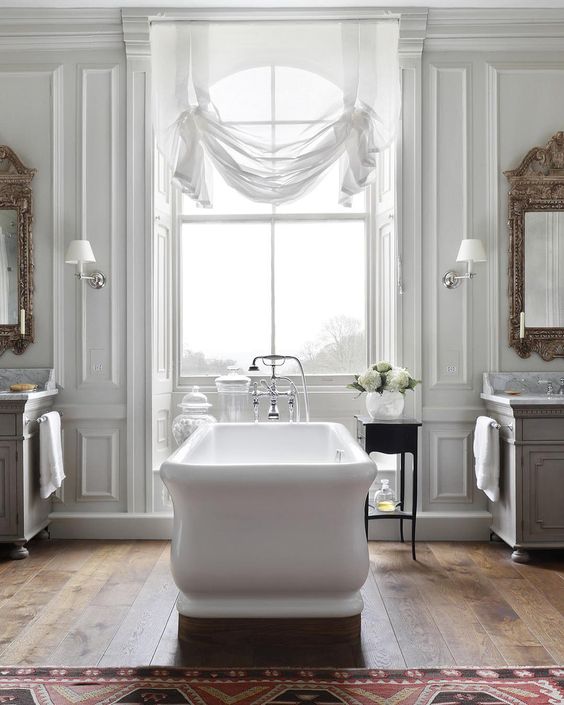 a beautiful vintage-inspired bathroom with a white tub, curtain, mirrors and chic vanities plus a rug