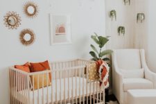 a boho chic nursery with potted greenery, a wooden crib and little rocker, a gallery wall and some boho rugs