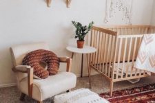 a bright boho nursery with a red boho rug, a white Moroccan pouf, macrame, mid-century shelves and a chic chair