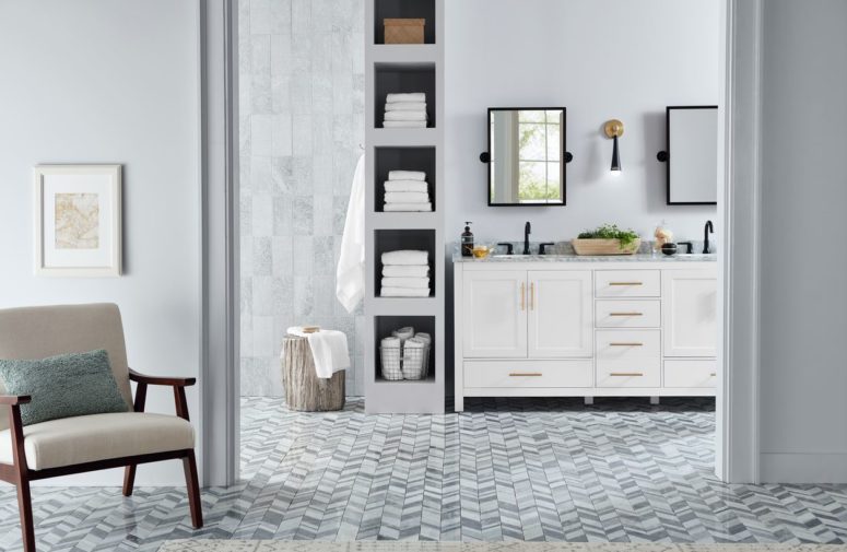 a chic transitional bathroom done with marble tiles, chevron clad floor tiles and a traditional vanity with a marble countertop