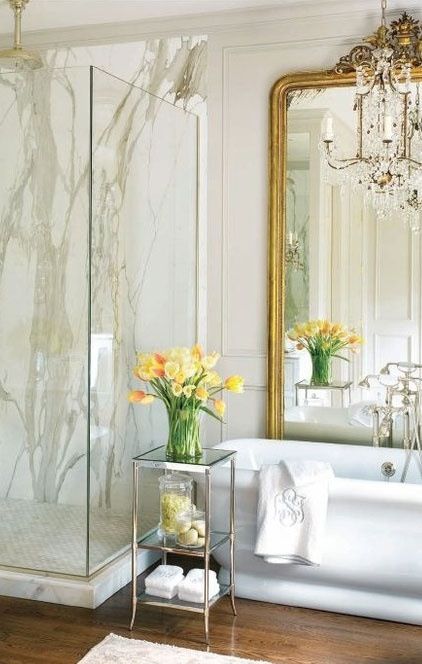 a chic vintage bathroom with white stone tiles, paneling, a sstatement mirror and a crystal chandelier a chic vintage bathroom with white stone tiles, paneling, a sstatement mirror and a crystal chandelier
