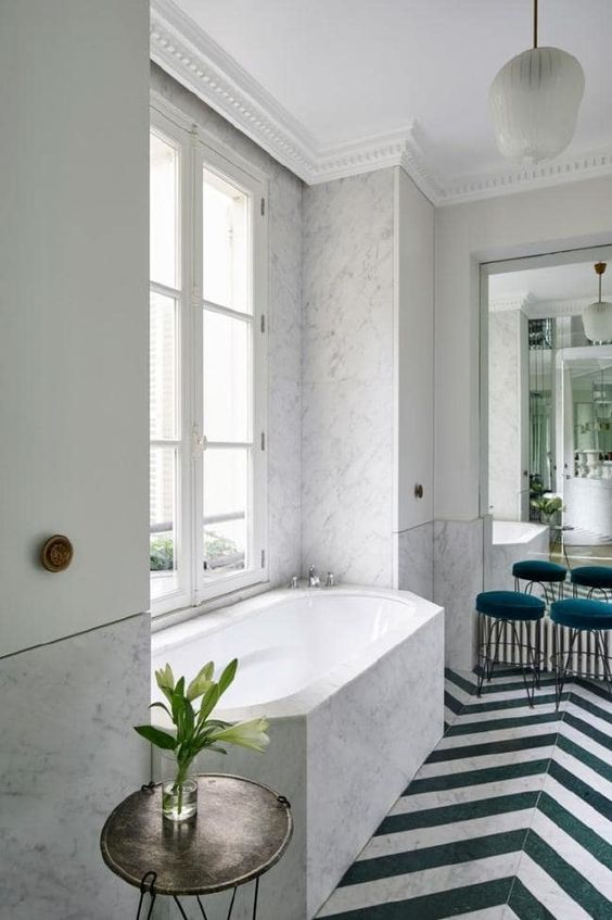 a contemporary Parisian bathroom done with white marble, chevron clad floor, teal stools and cabinets on the walls