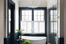 a contemporary Parisian bathroom with an oval tub, a large crystal chandelier, black and white walls and a hex tile floor