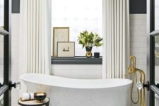 a glam Parisian bathroom with a mosaic tile floor, a clawfoot bathtub, a statement chandelier, gold touches and artworks