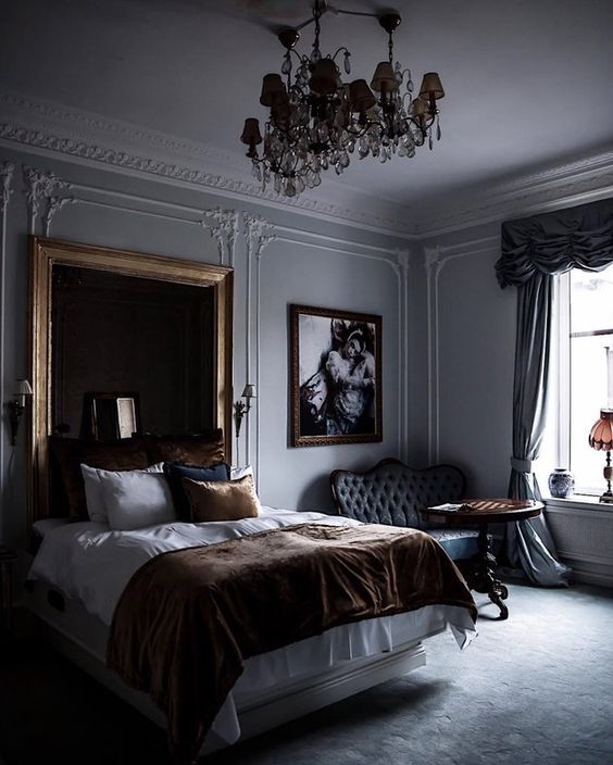 a moody refined bedroom with a statement chandelier, artworks, stucoo, a dark upholstered headboard and sophisticated furniture