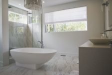 a neutral transitional bathroom with marble tiles on the floor and in the shower and a luxurious modern chandelier