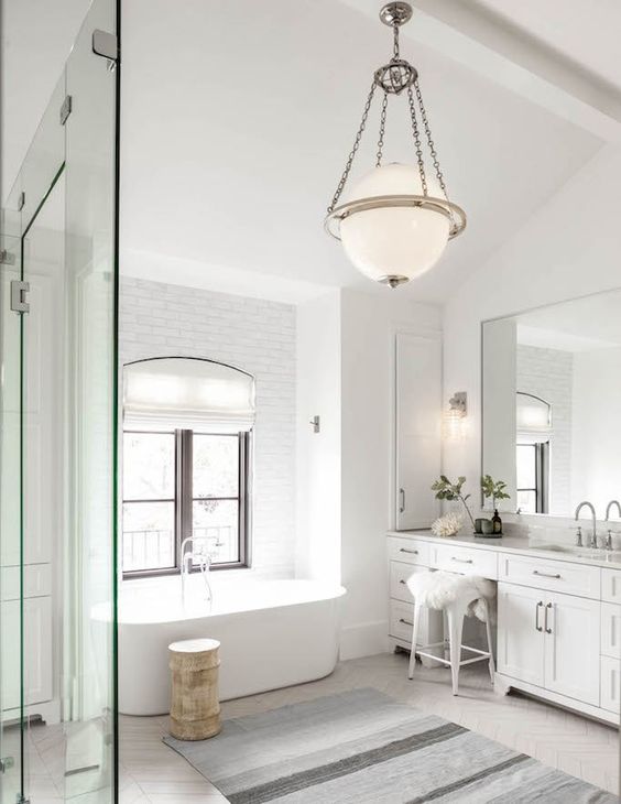 a neutral transitional space with a modern tub, a catchy pendant lamp, a striped rug and a chic vintage vanity with drawers