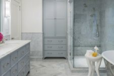 a relaxing bathroom done in greys and neutrals, with a chic chandelier, stylish vintage storage units and marble tiles