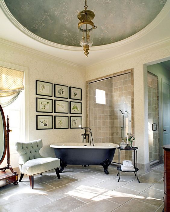 a stylish vintage bathroom with a gallery wall, a black clawfoot tub, a unique pendant lamp and some elegant furniture