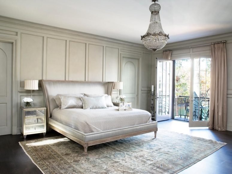 a very elegant Parisian bedroom with a printed rug, a chic upholstered bed, a crystal chandelier and mirror nightstands