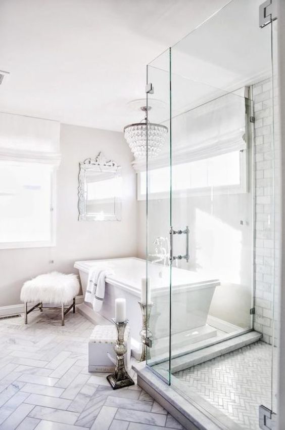 an ornate mirror, a crystal chandelier, a faux fur stool and candles plus marble tiles make the bathroom glam