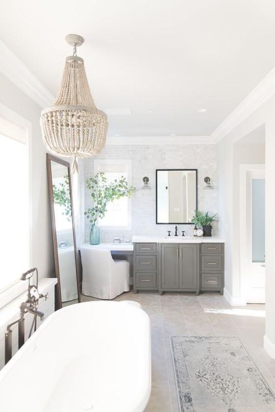 combining a vintage vanity with a contemporary tub, a bead chandelier, a large vintage mirror and a printed rug
