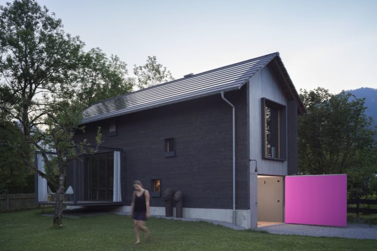 This holiday home is small and tall, with black exterior walls and a bright pink garage door
