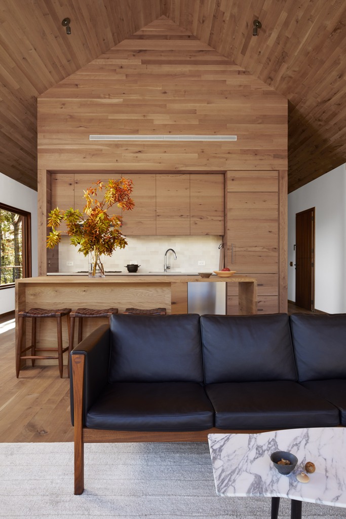 The kitchen is done with sleek wooden cabinets, a large kitchen island, woven stools, and a neutrla backsplash and it seamlessly flows into the living room