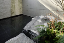 04 The inner patio is done with sleek black tiles, ferns, a tree and natural rocks that contrast the tiles very much