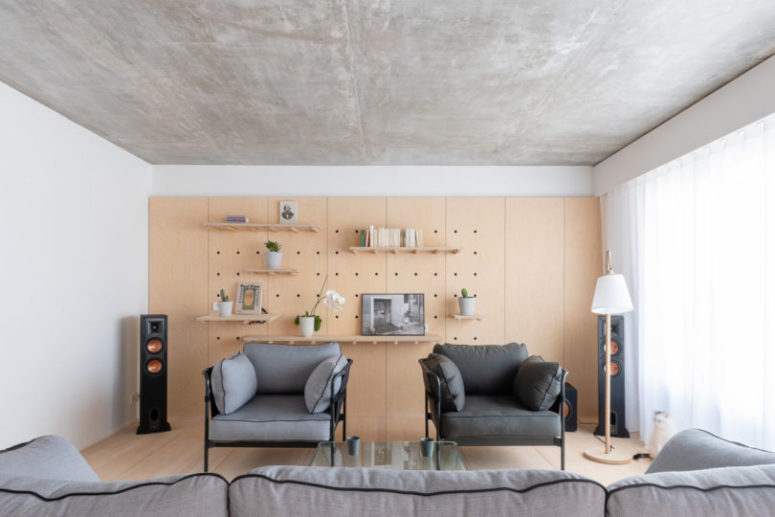 The living room is done with a pegboard wall with shelves, a couple of chairs and a matching sofa plus a glass table