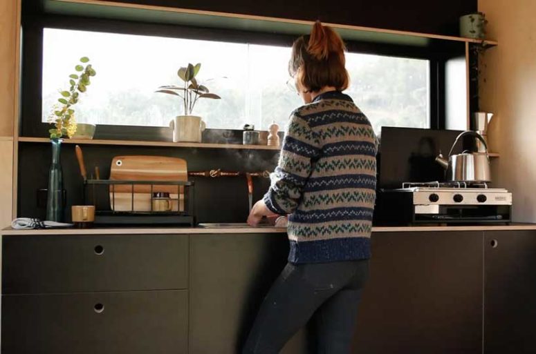 The kitchen is done with grey plywood cabinets, some shelves and a window to enjoy the views while cooking