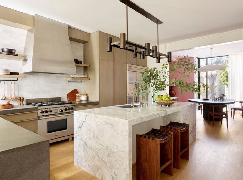 The kitchen is done with neutral plywood cabinets, a marble kitchen island and a cool track lighting fixture