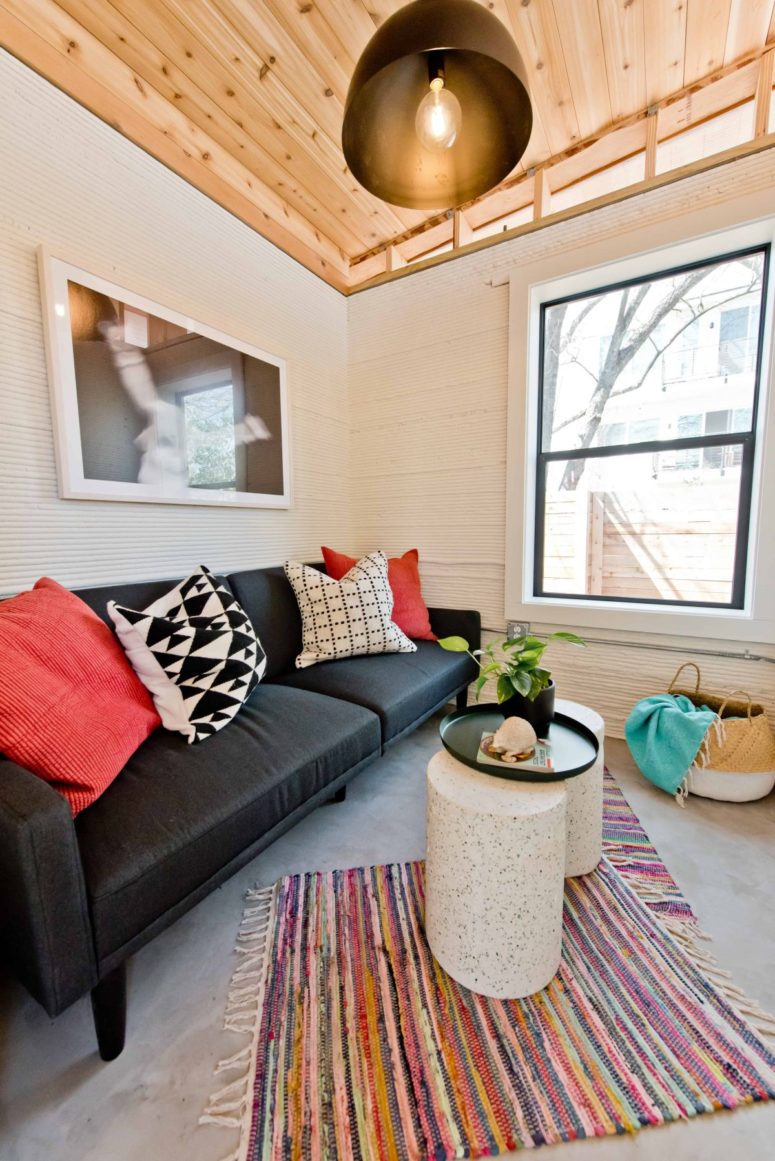The living room features a black sofa, white side tables, a metal lamp and an artwork plus colorful rugs The living room features a black sofa, white side tables, a metal lamp and an artwork plus colorful rugs
