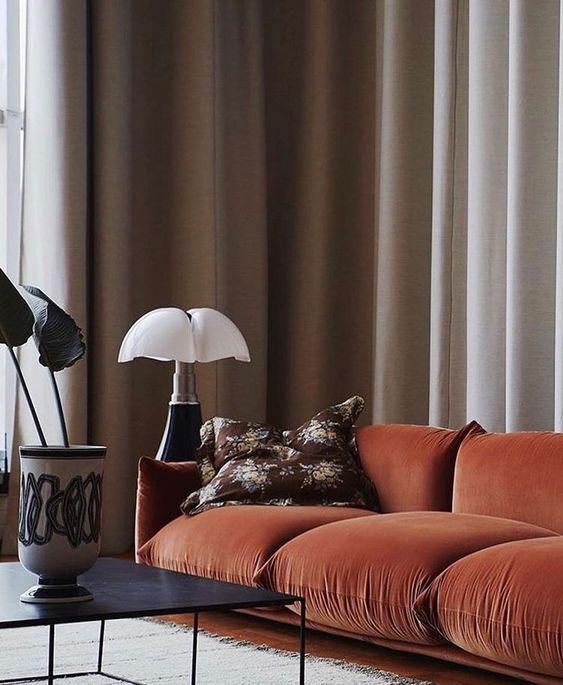 a bold rust colored velvet sofa with soft cushions and pillows will brighten up your living room