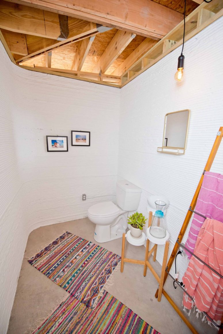 The bathroom is small and is done with simple stands, a ladder for towels and colorful rugs