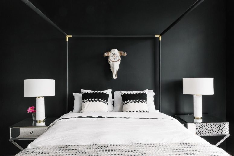 a gorgeous bedroom with black walls, a framed bed, mirror nightstands and a skull on the wall