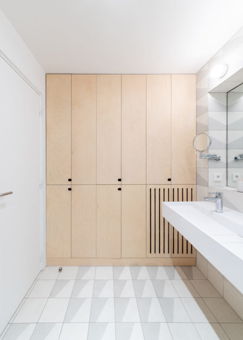 The bathroom continues the decor of the apartment with sleek plywood cabinets and neutral tiles