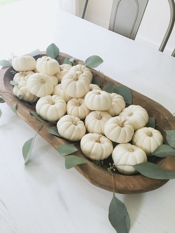 a pretty fall centerpiece of a wooden dough bowl filled wiht white pumpkins and greenery