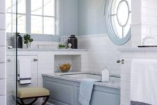 a beautiful light blue and white bathroom with marble and subway tiles, a porthole window nd a usual one