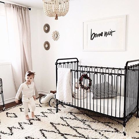 a black and white nursery with a printed rug, a black bed, a bead chandelier and a simple artwork